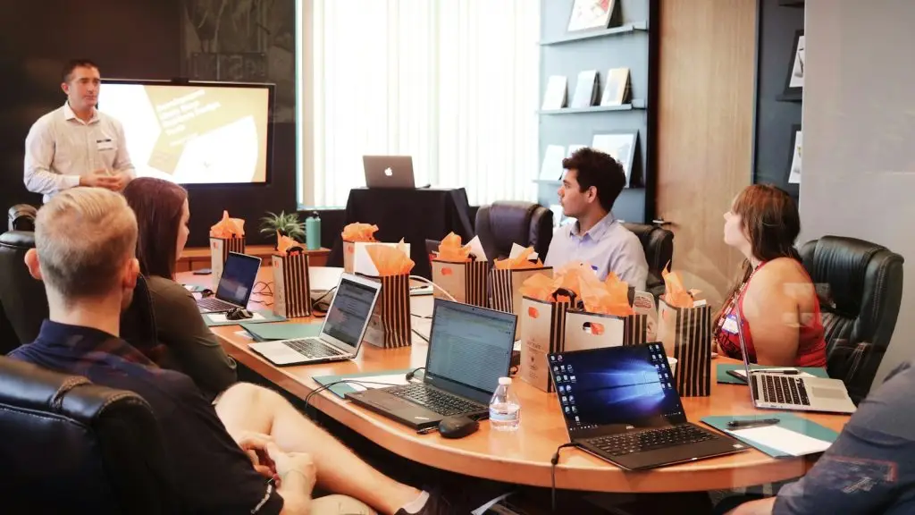 A business leader presenting a plan to a team seated around a table with laptops