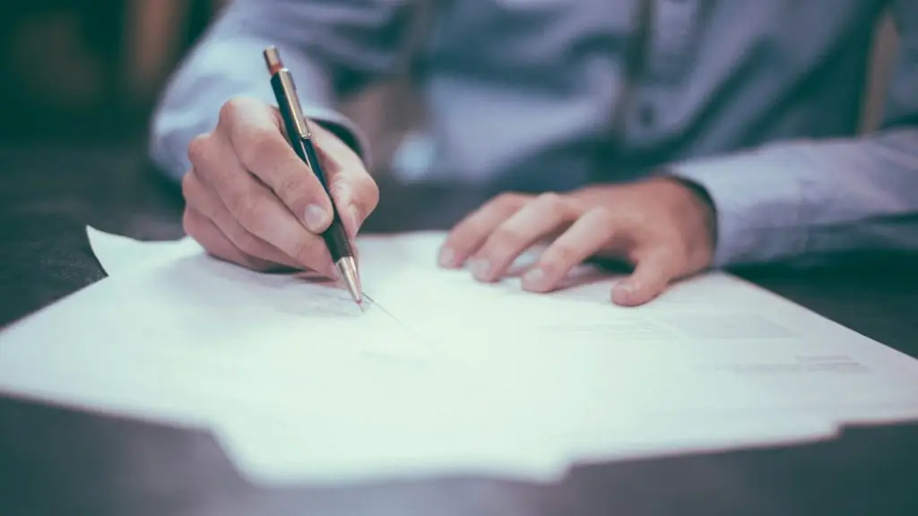 A person signing a contract at a desk, with pen and papers